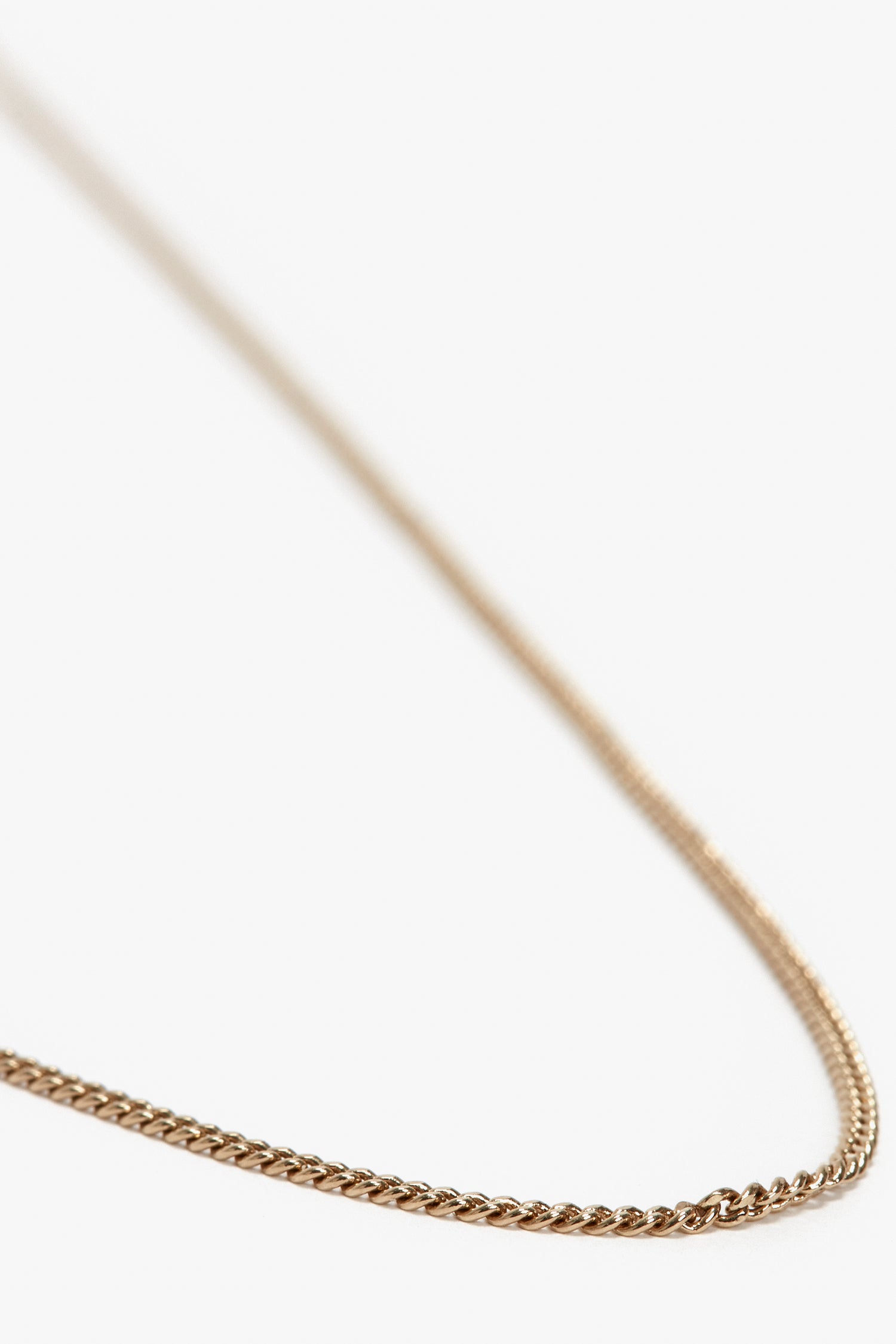 Close-up of a fine, gold-plated brass chain necklace against a white background. The slender chain features a detailed, interwoven pattern, adorned with the Victoria Beckham logo. This is the Exclusive Long Fine Chain In Gold by Victoria Beckham.