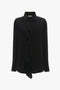 Victoria Beckham's Asymmetric Ruffle Blouse In Black, with long sleeves and a classic collar, is displayed on a plain white background.