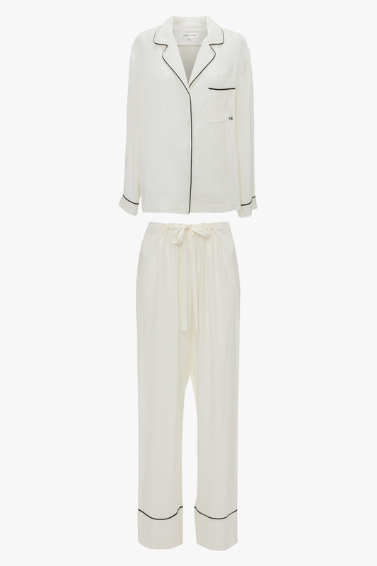 A **Victoria Beckham VB Monogram Pyjama Sleep Set In Ivory**. The top features long sleeves, a collar, and a chest pocket, while the pants have an elastic waistband with a drawstring.