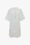 A white Victoria Beckham Frame Cut-Out T-Shirt Dress In White, with a keyhole neckline, front slit, and pleated hem.