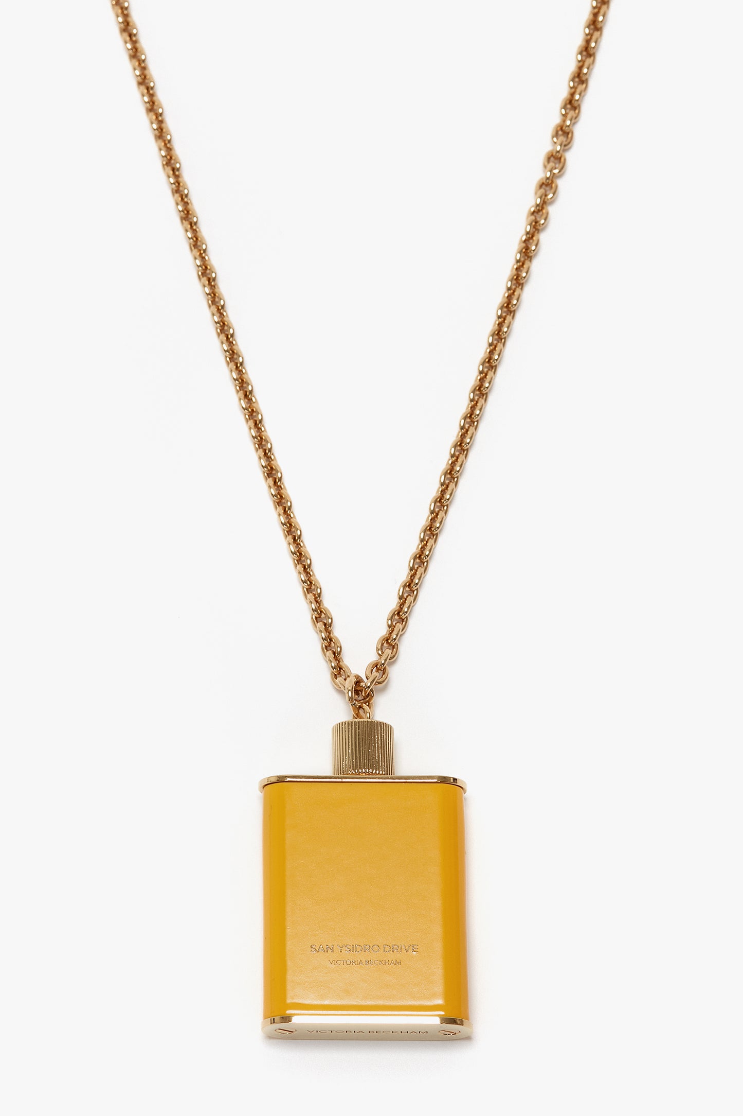 A gold-colored necklace featuring a small, rectangular pendant designed to resemble a flask in gold brushed brass. The pendant is inscribed with "San Ysidro Drive," "1947," and "Gold Label Reserva Especial." This unique jewellery piece exudes elegance, reminiscent of the Perfume Bottle Necklace In San Ysidro Drive by Victoria Beckham branding.