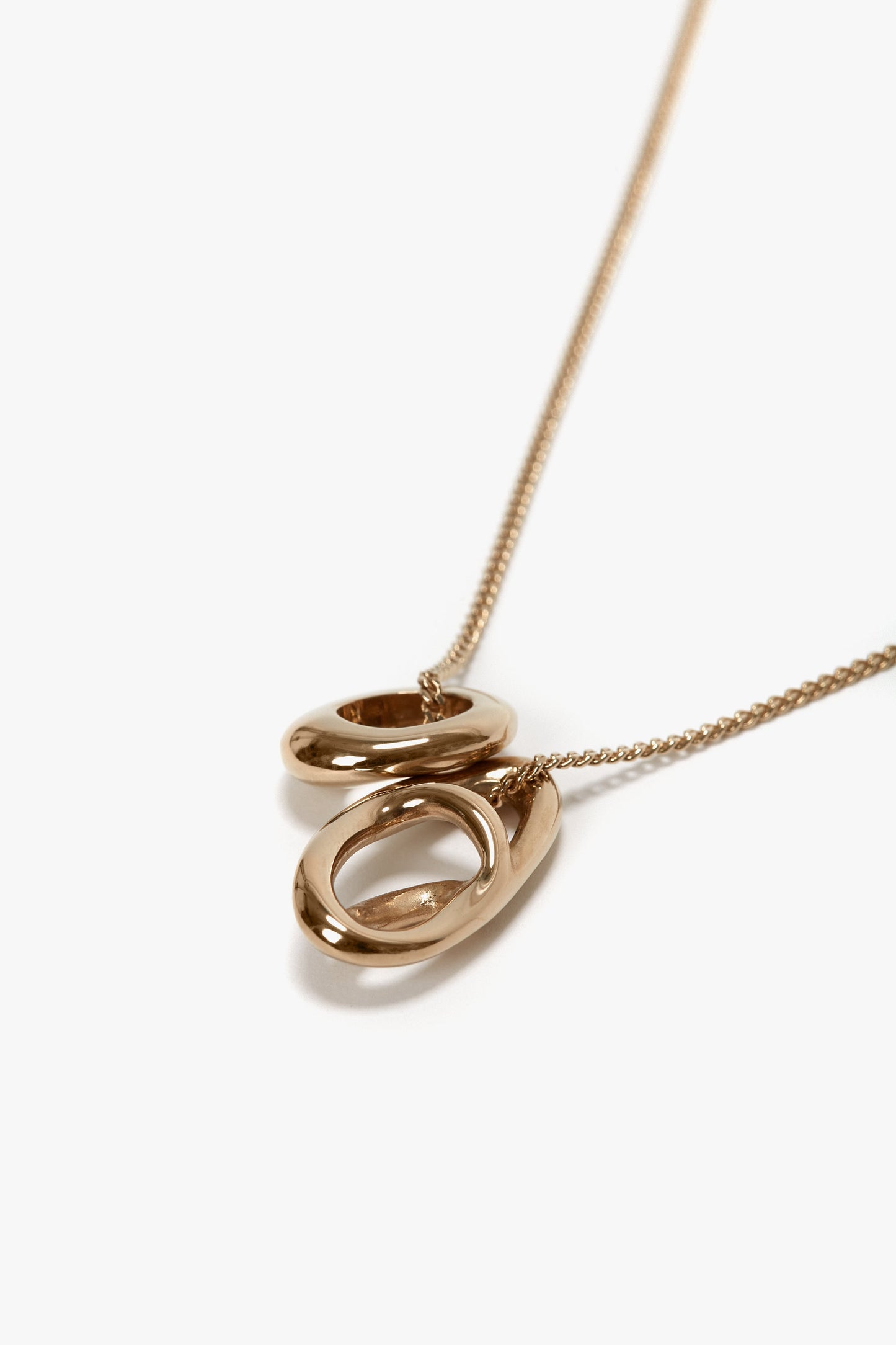 A Victoria Beckham Exclusive Abstract Charm Necklace In Light Gold featuring two interlocking oval rings on a delicate chain against a white background, crafted from 100% brass.