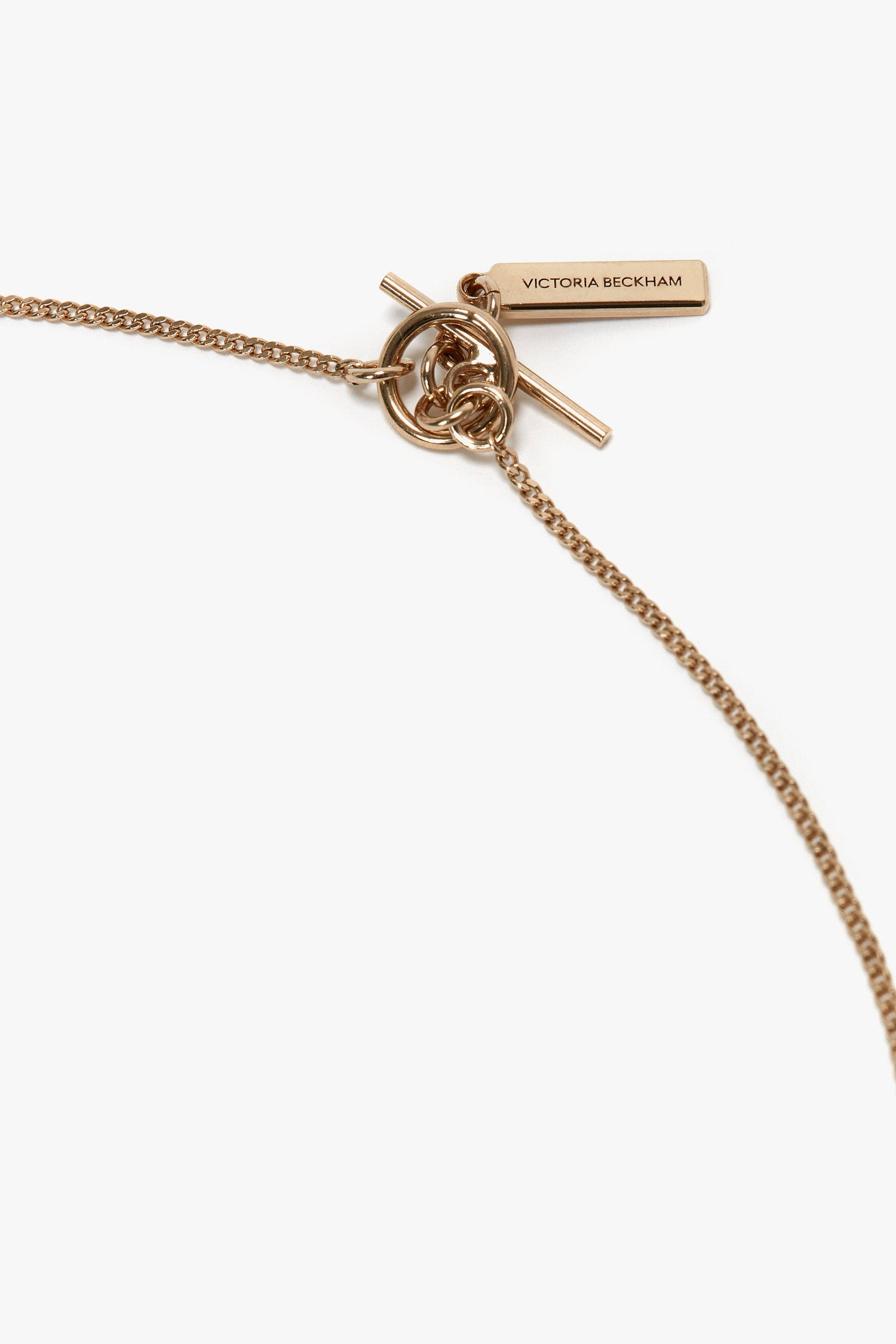 Close-up of an Exclusive Abstract Charm Necklace In Light Gold with a T-bar clasp and an abstract charm tag engraved with "Victoria Beckham," made from 100% brass.