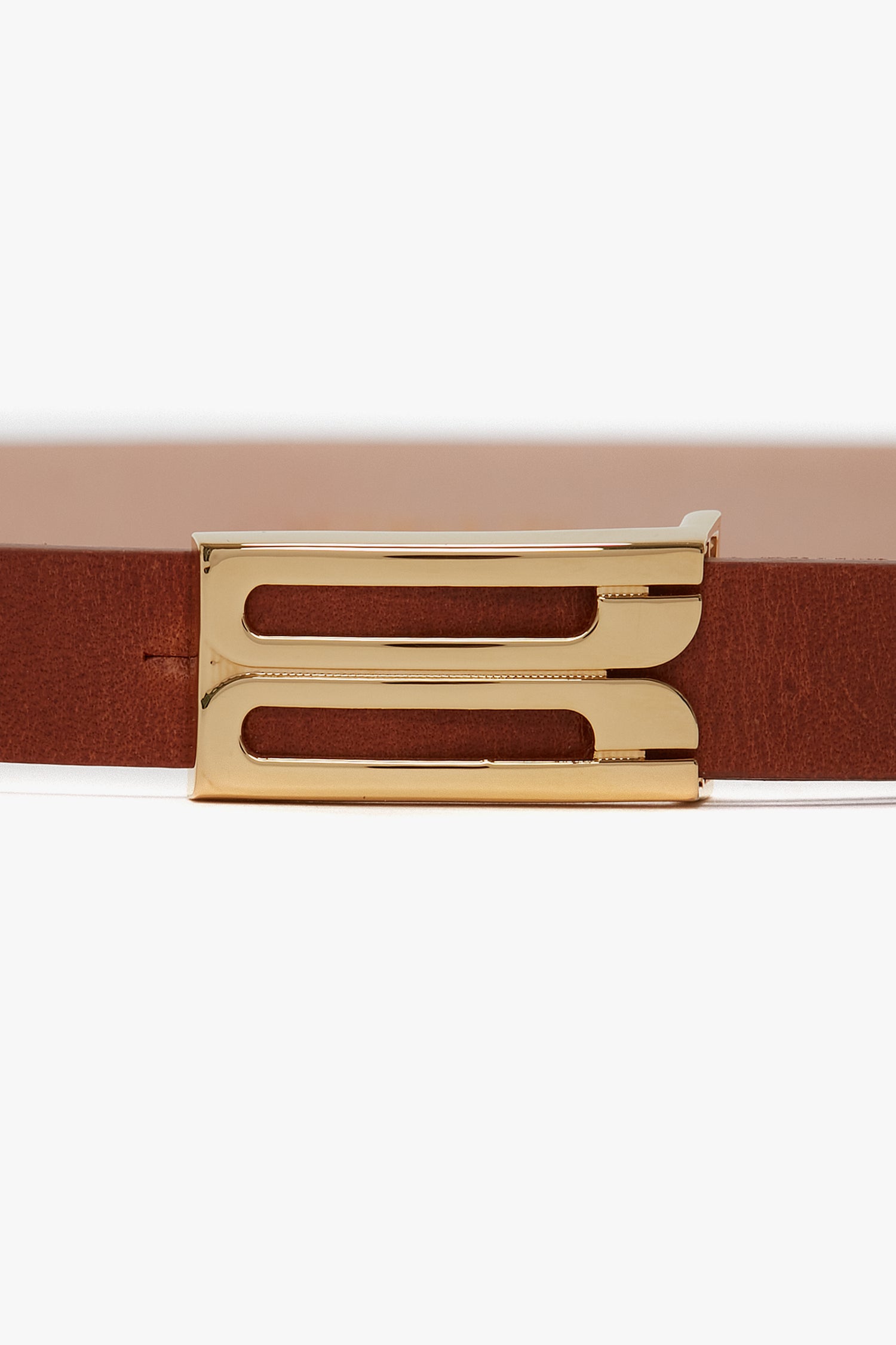 Close-up of the Exclusive Micro Frame Belt In Tan Leather by Victoria Beckham, crafted from smooth calf leather, with a unique gold hardware buckle featuring a rectangular and angular design.