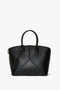 A Victoria Beckham Victoria Bag In Black Leather with structured leather panels, two top handles, and a zipper closure.