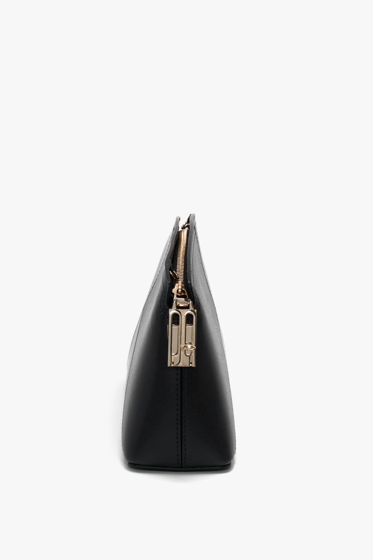 Side view of a black zippered Victoria Beckham Victoria Crossbody Bag In Black Leather, made from textured calf leather with gold hardware and an adjustable strap, against a white background.