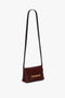 A Mini Chain With Long Strap Pouch Bag In Burgundy Leather by Victoria Beckham, featuring a gold chain detail on the flap.