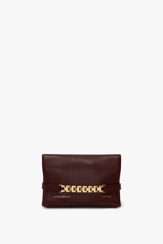 A rectangular, dark brown leather clutch bag with a gold chain detail and a detachable strap, featuring a flap closure has been replaced by the Mini Chain With Long Strap Pouch Bag In Burgundy Leather by Victoria Beckham.