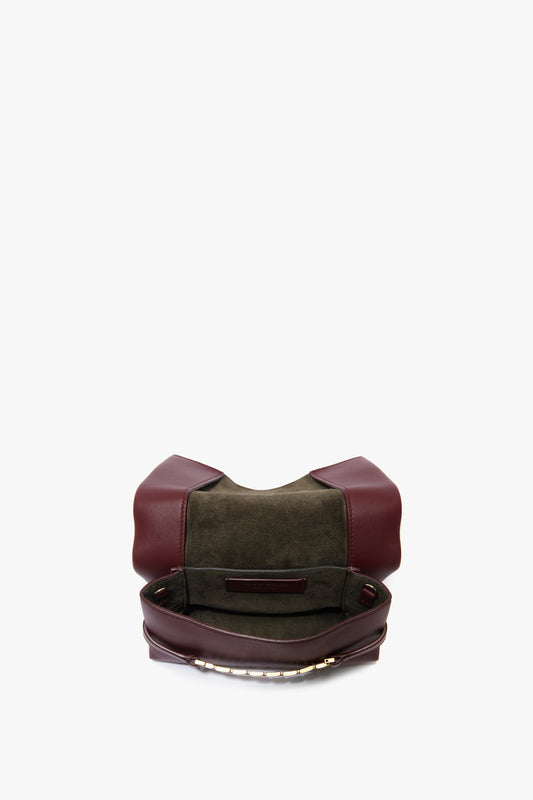 A burgundy leather bag with an open top, revealing a dark green suede interior and a small inner pocket. This elegant accessory features a Mini Chain With Long Strap Pouch Bag In Burgundy Leather by Victoria Beckham for versatile styling options.