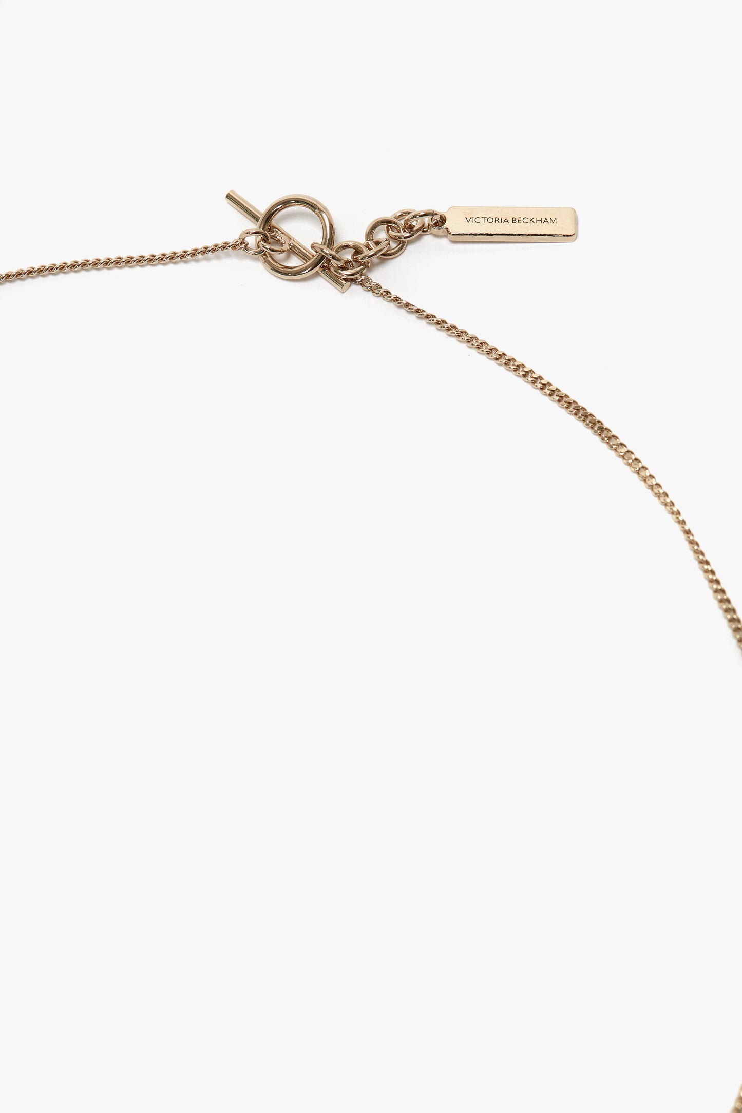 A close-up view of an Exclusive Resin Pendant Necklace in Light Gold-Black featuring a T-bar closure and a rectangular tag engraved with "Victoria Beckham".