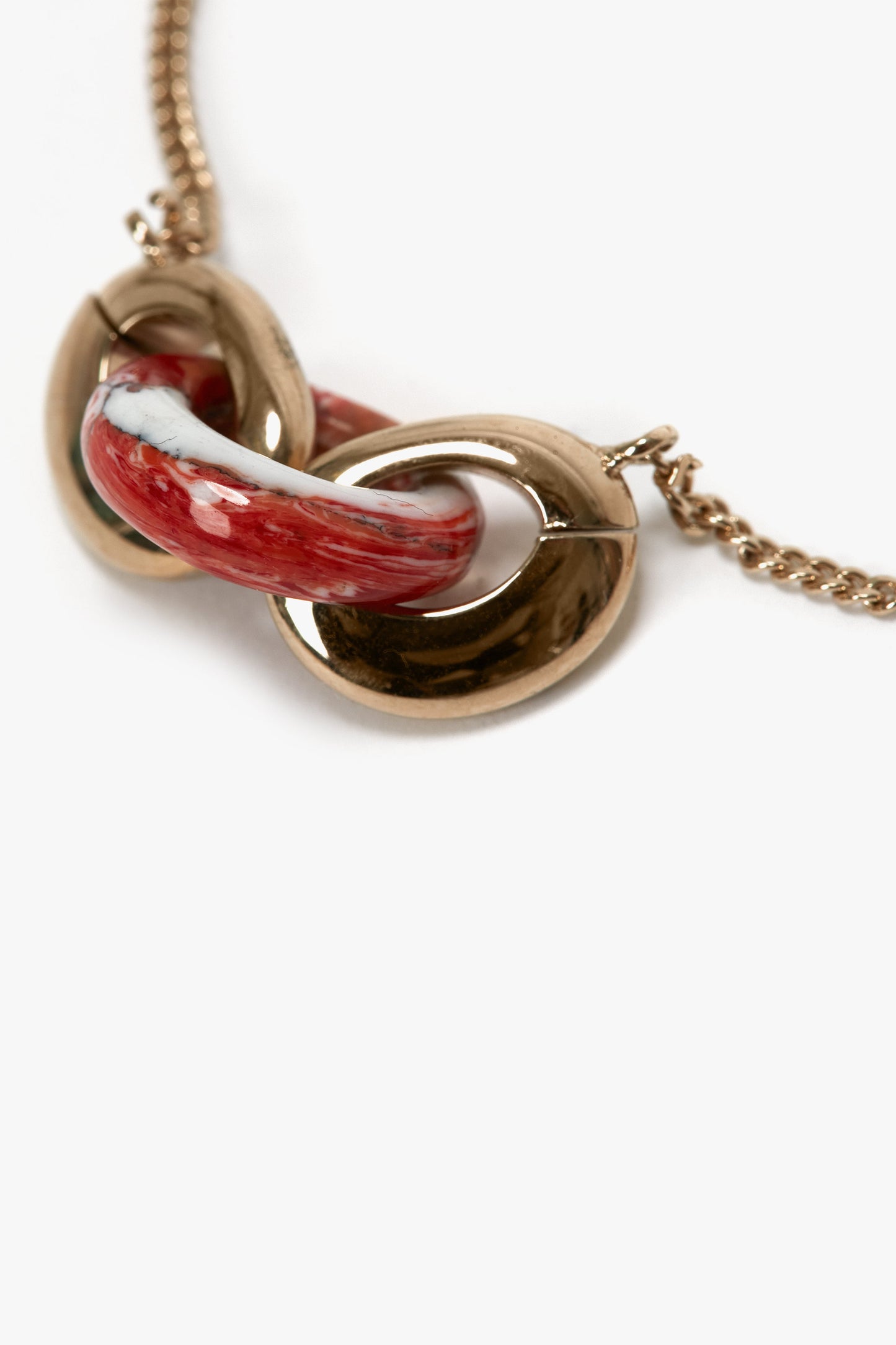 Close-up of a Victoria Beckham Exclusive Resin Charm Bracelet In Light Gold-Orange with an interlocking red and white enamel pendant. The pendant, reminiscent of a resin charm bracelet, appears to be comprised of two curved sections intertwined together.