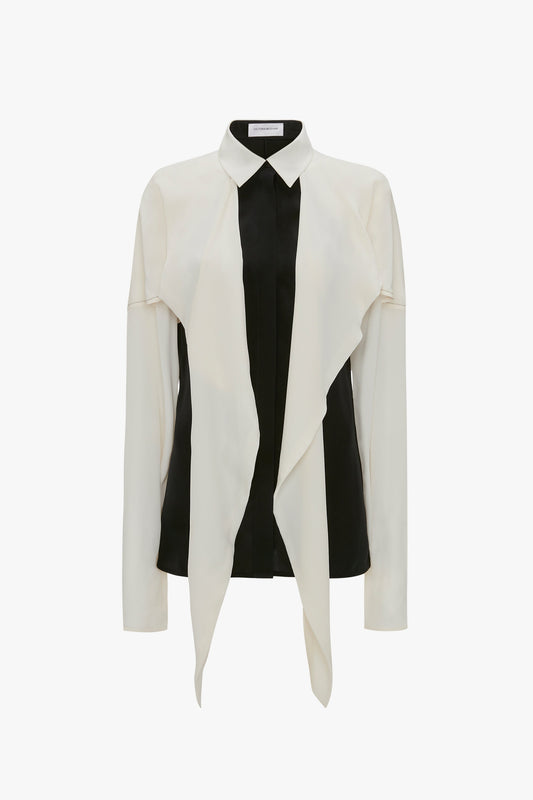 The Victoria Beckham Oversized Bow Detail Blouse In Vanilla is a long-sleeved blouse with a cream draped front and black panels on the sides, featuring an oversized bow detail for a feminine flourish under a buttoned front closure.