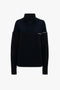 A navy Collar Detail Jumper by Victoria Beckham with a high ribbed collar, long sleeves, and a distinct pattern change below the collar offers a contemporary perspective on classic design.