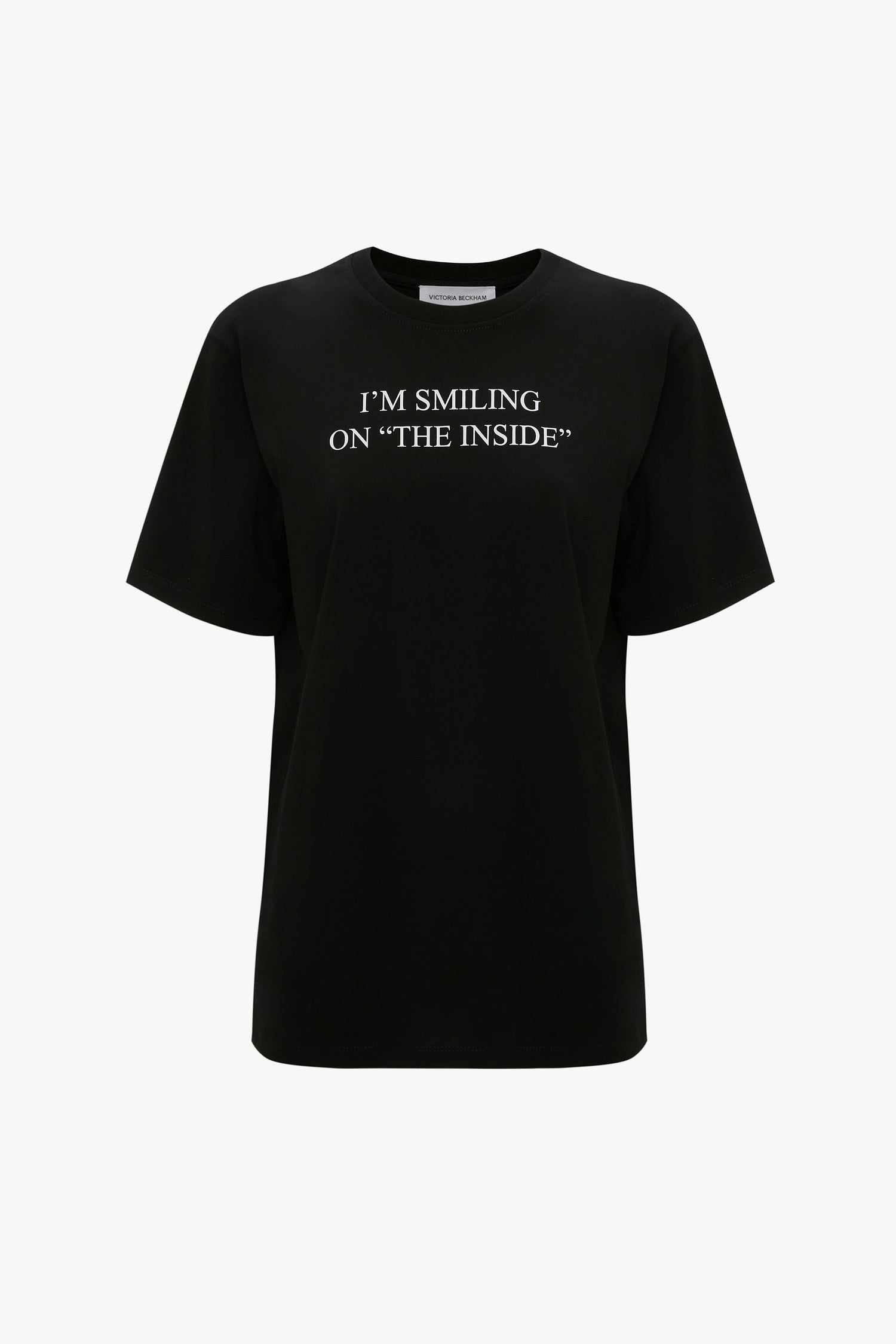 I'm Smiling On The Inside Slogan T-Shirt in Black by Victoria Beckham with white text that reads "I'M SMILING ON 'THE INSIDE'" displayed on a plain white background. Made from organic cotton for a relaxed fit.