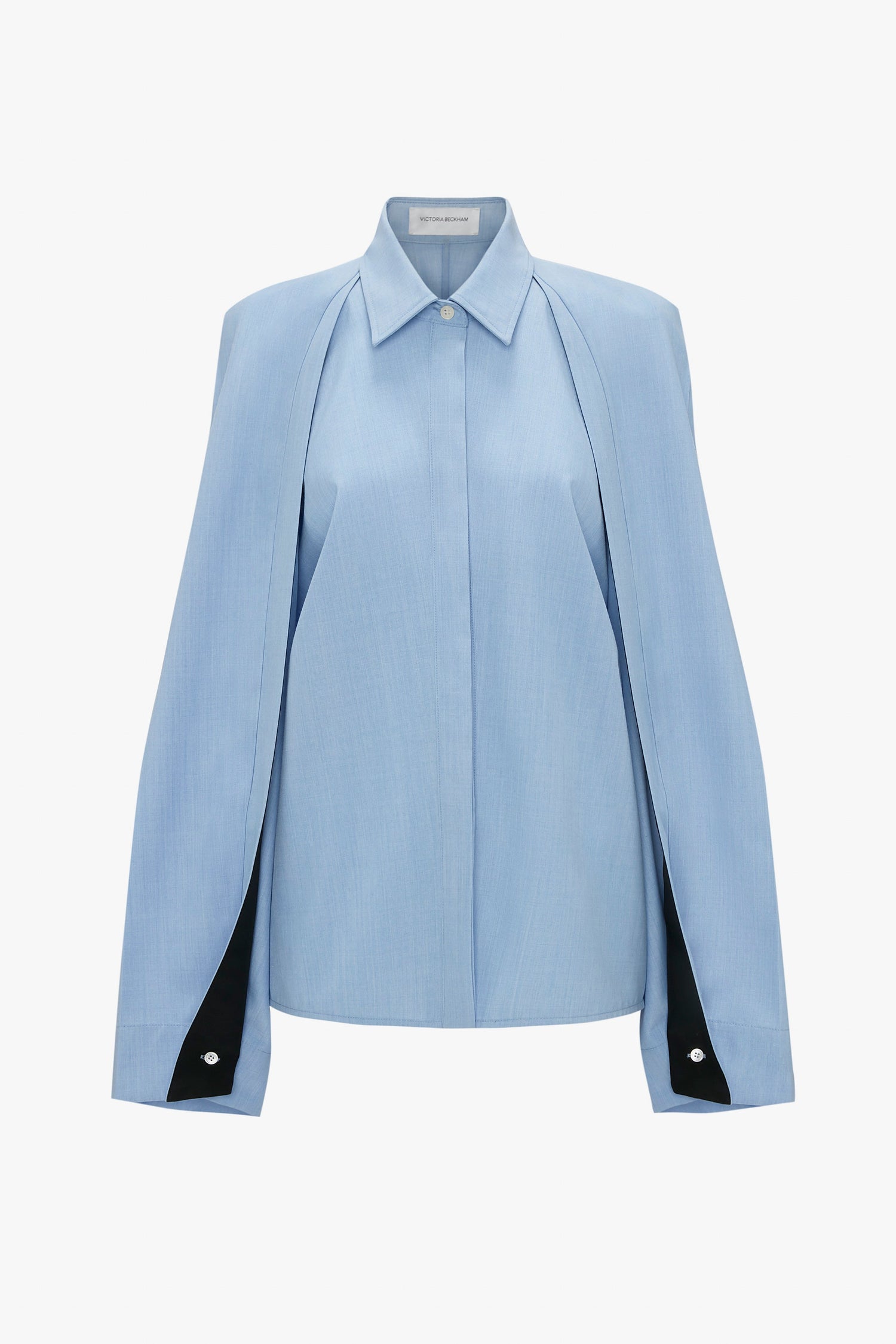 A light blue blouse with a cape-like design, long sleeves, and elegant button details at the cuffs. The Pleat Detail Raglan Shirt In Oxford Blue by Victoria Beckham also features raglan sleeves, adding a modern twist to its timeless style.