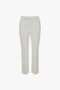 A pair of Cropped Kick Trousers In Ivory by Victoria Beckham with belt loops and stitched seams, shown flat on a white background.