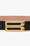 A Jumbo Frame Belt In Black Leather with a gold rectangular buckle featuring two elongated cut-out designs, crafted from smooth calf leather by Victoria Beckham.