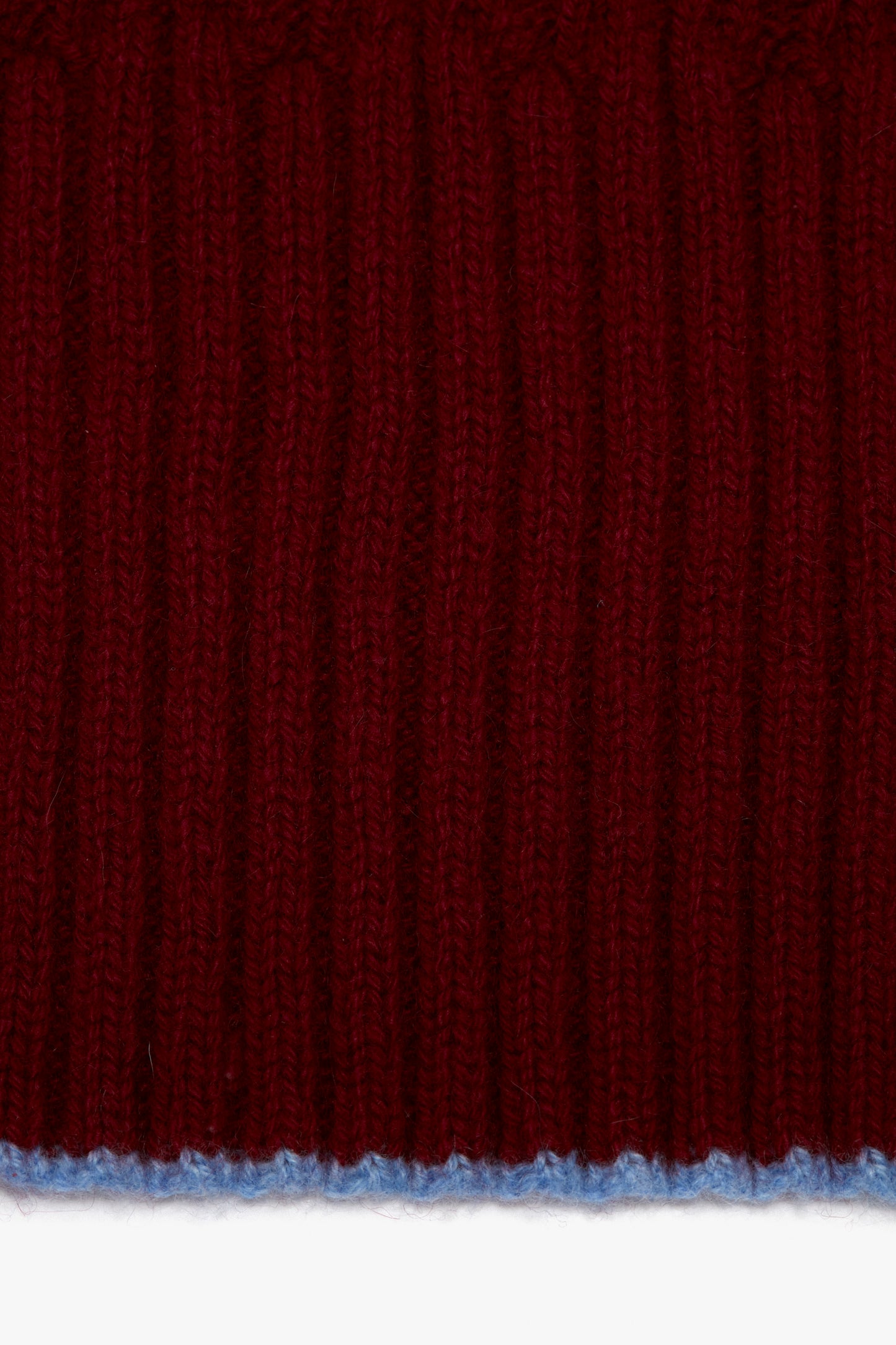 Close-up of a red knitted luxury scarf with distinct vertical ribbing and a thin blue thread at the bottom edge featuring a Victoria Beckham logo.