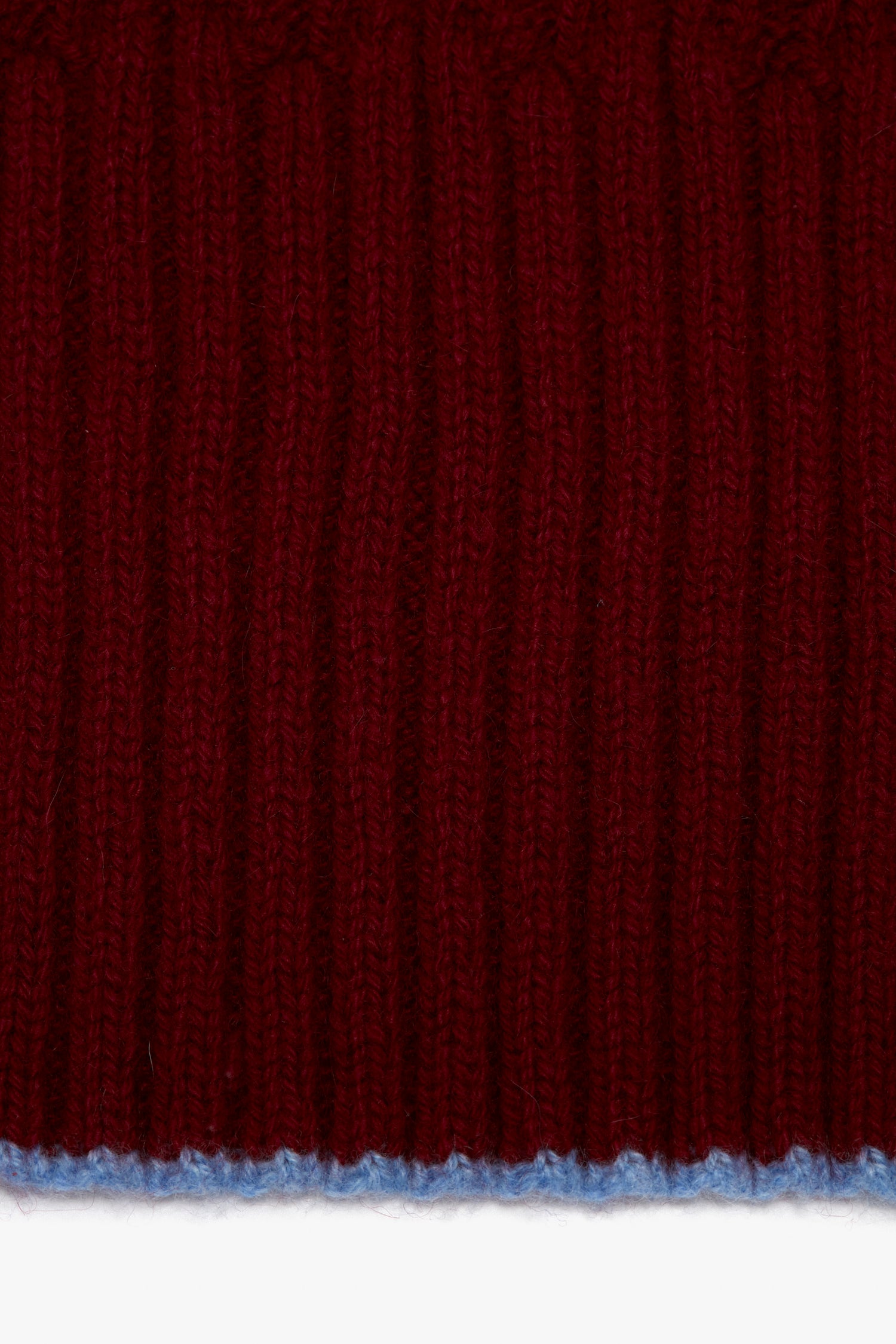 Close-up of a red knitted luxury scarf with distinct vertical ribbing and a thin blue thread at the bottom edge featuring a Victoria Beckham logo.