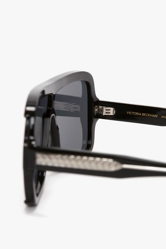 Close-up of Layered Mask Sunglasses In Black-Silver-Mirror with dark lenses, featuring the brand name "Victoria Beckham" on the temple. The rectangular shape and guilloch pattern on the hinges and detailing are clearly visible.