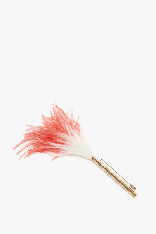 A Victoria Beckham Feather Brooch In White-light gold/cream-red with pure ostrich feather plumes in red and white, and a gold-plated brass handle, placed on a white background.