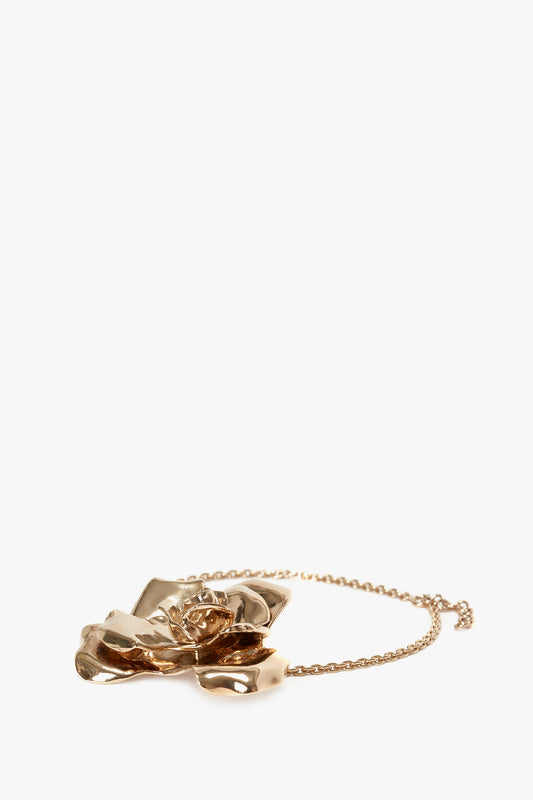 An Exclusive Flower Necklace In Gold featuring a large, intricately designed flower pendant crafted from gold brushed brass on a fine chain, set against a plain, white background. This statement accessory from Victoria Beckham adds an elegant touch to any outfit.