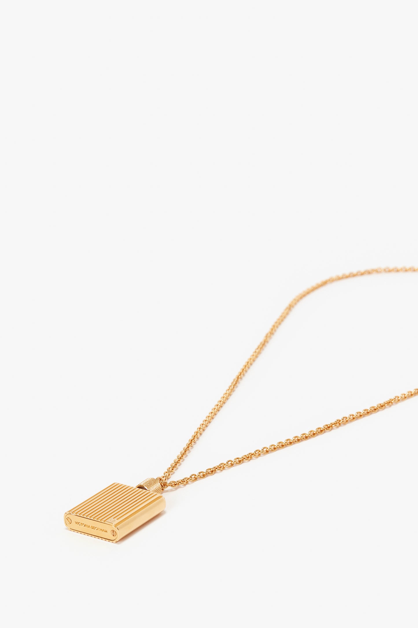 Victoria Beckham's Exclusive Perfume Bottle Necklace In Brushed Gold featuring a rectangular, gold brushed brass pendant with vertical stripes placed against a white background.