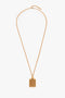 A Victoria Beckham Exclusive Perfume Bottle Necklace In Brushed Gold with a rectangular-shaped pendant featuring vertical lines, reminiscent of a perfume bottle pendant necklace, displayed on a white background.