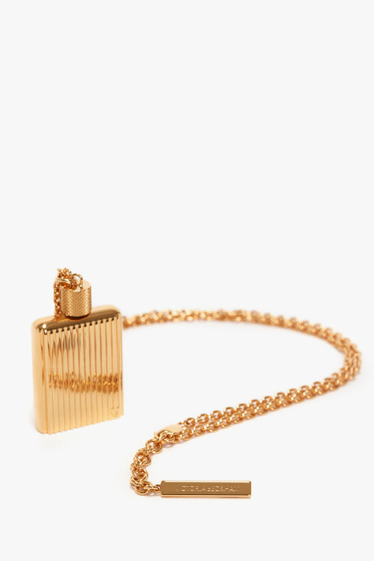 A gold brushed brass rectangular pendant flask with a ribbed design and a secure clasp sits attached to a matching gold chain, creating the perfect Exclusive Perfume Bottle Necklace In Brushed Gold for showcasing Victoria Beckham parfums.