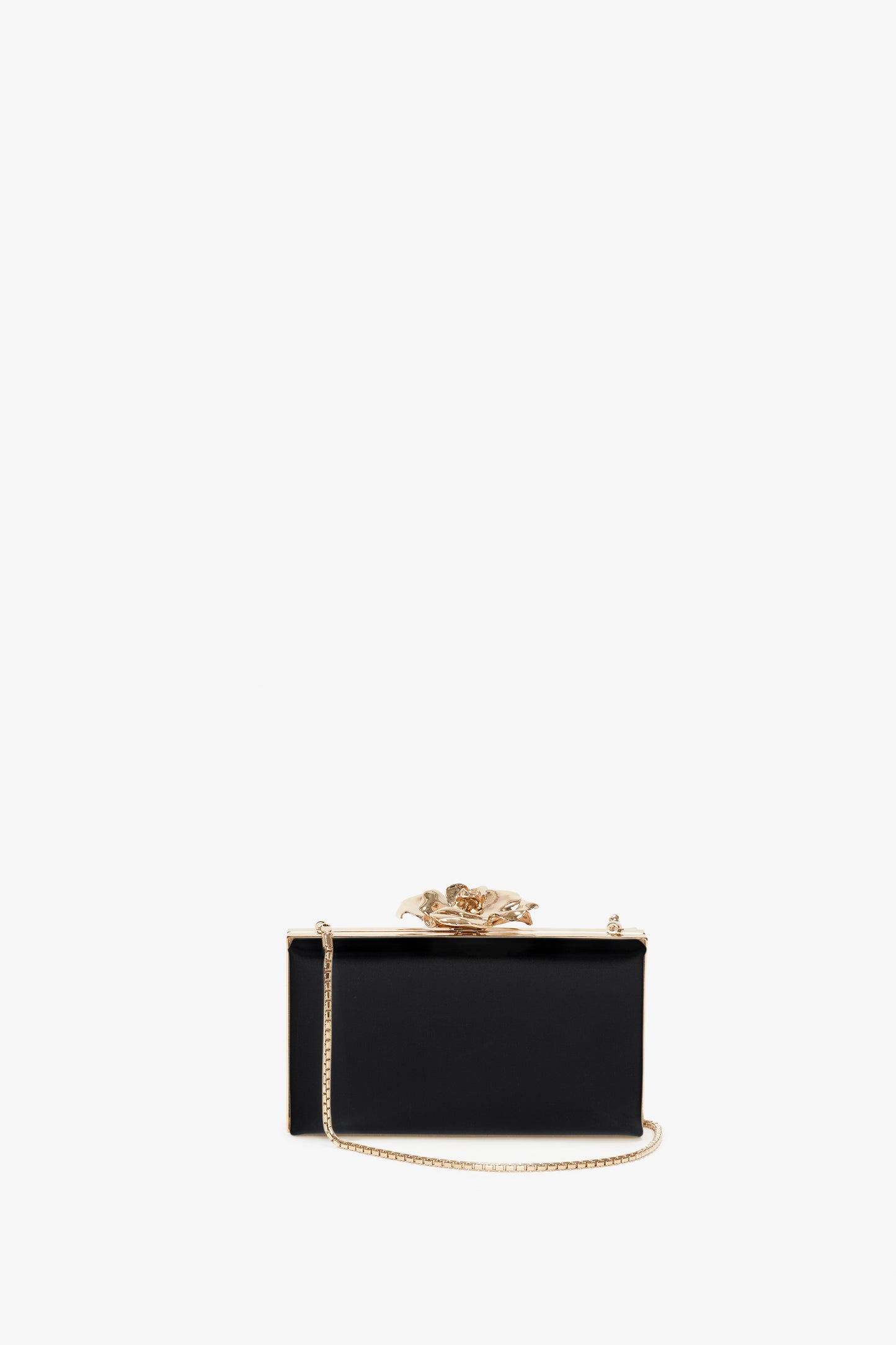 A small black Frame Flower Minaudiere Bag in Black by Victoria Beckham with a bespoke brass frame and an exquisite flower clasp is centered against a white background, complemented by a gold chain shoulder strap.