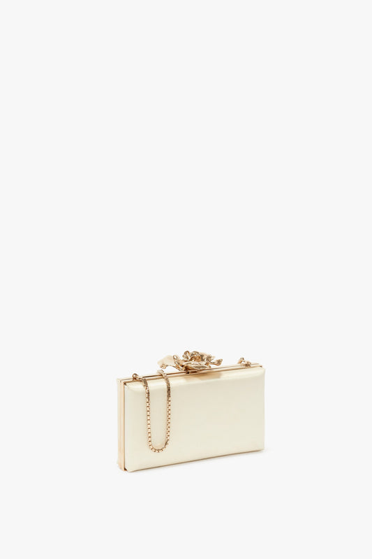 A rectangular, ivory Frame Flower Minaudiere in Bag Chamomile by Victoria Beckham with gold hardware and a chain strap, adorned with a decorative floral clasp on top. This exquisite accessory adds an elegant touch to any outfit.