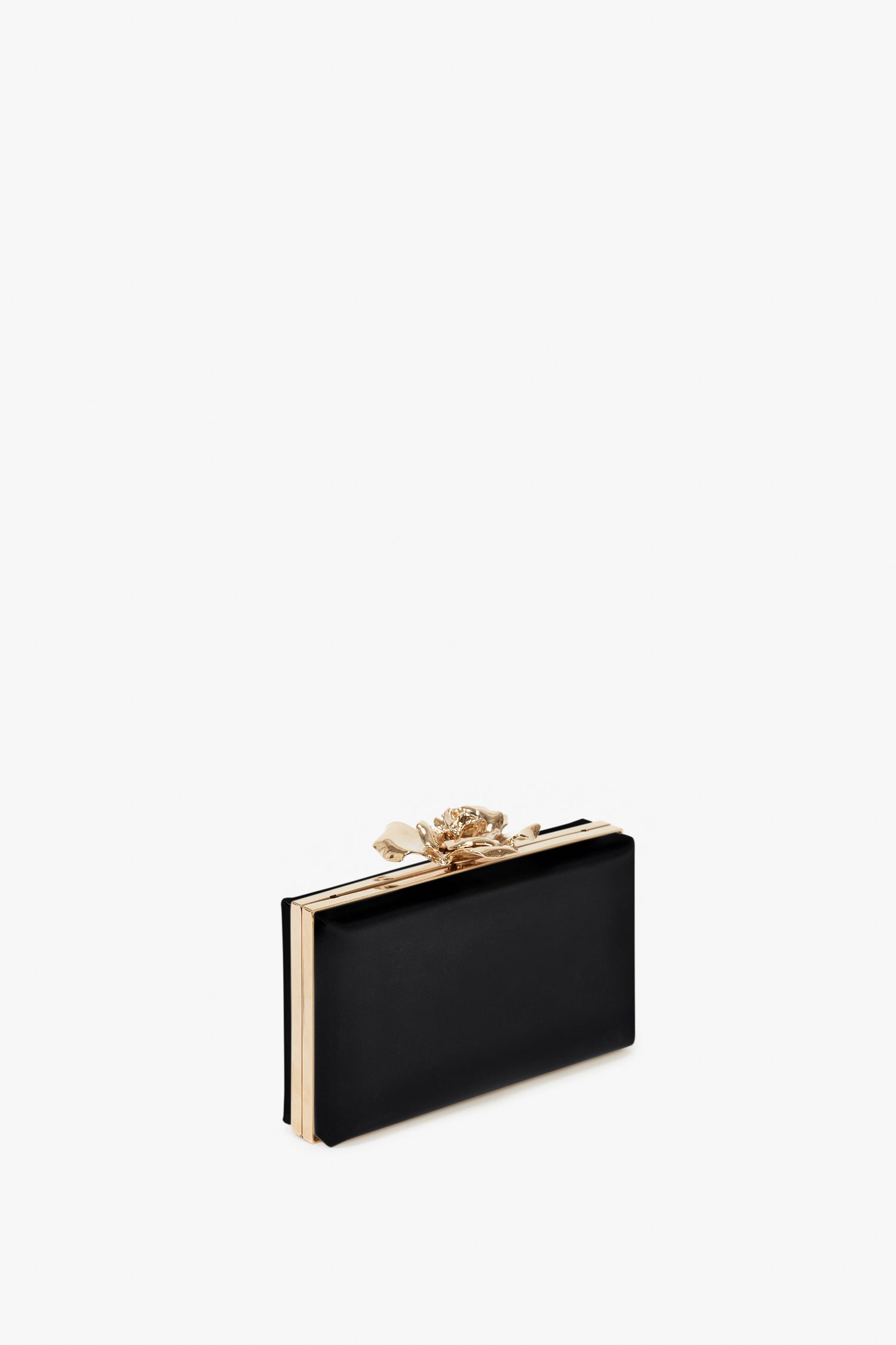 A rectangular black hand-crafted Frame Flower Minaudiere Bag in Black with a bespoke brass frame and a gold bow on top, set against a white background by Victoria Beckham.