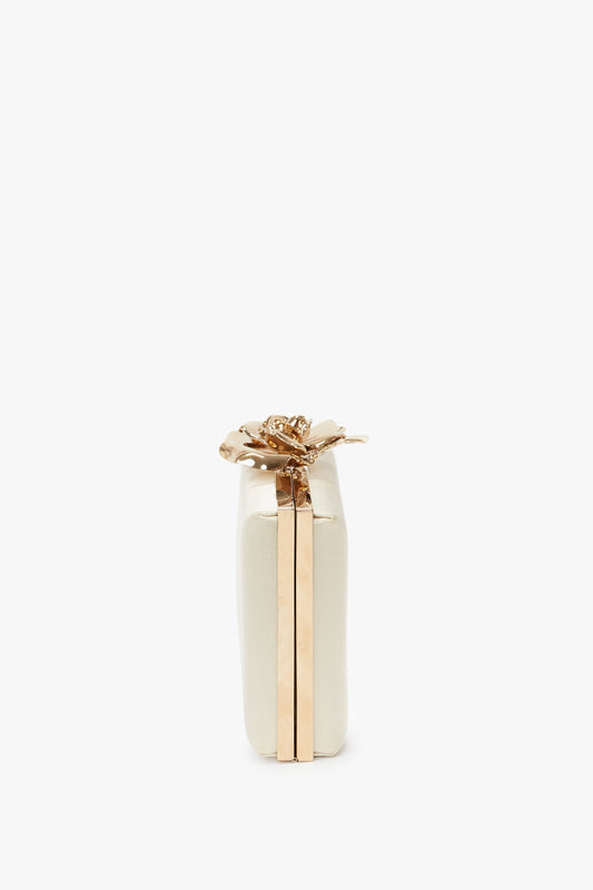 Side view of a white rectangular Frame Flower Minaudiere in Bag Chamomile with gold accents, featuring a decorative gold flower clasp on the top—an elegant accessory reminiscent of Victoria Beckham's timeless style.