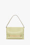 A light yellow Chain Pouch Bag With Strap In Avocado Leather by Victoria Beckham with a wide shoulder strap and a decorative gold chain detail on the front.