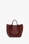 A large, dark red leather handbag crafted from grained leather with dual handles, an open top, and a structured shape featuring subtle stitch details. The **Victoria Beckham W11 Medium Tote Bag In Burgundy Leather** combines elegance and functionality perfectly.