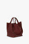 A Victoria Beckham W11 Medium Tote Bag In Burgundy Leather, featuring two handles and an adjustable shoulder strap, all set against a pristine white background.