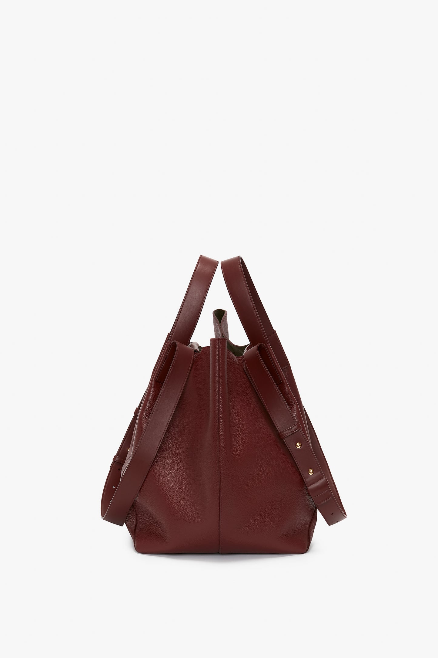 A W11 Medium Tote Bag In Burgundy Leather by Victoria Beckham with adjustable straps and gold-tone hardware, crafted from grained leather, stands upright on a plain white background.