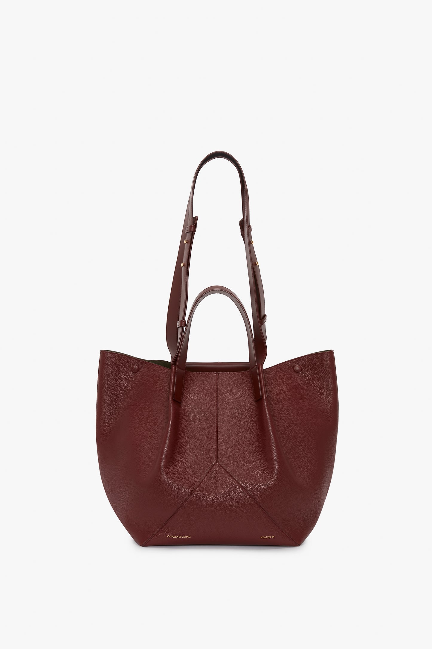 A W11 Medium Tote Bag In Burgundy Leather by Victoria Beckham with two long adjustable straps and two short handles, featuring a structured design and minimalistic aesthetic.