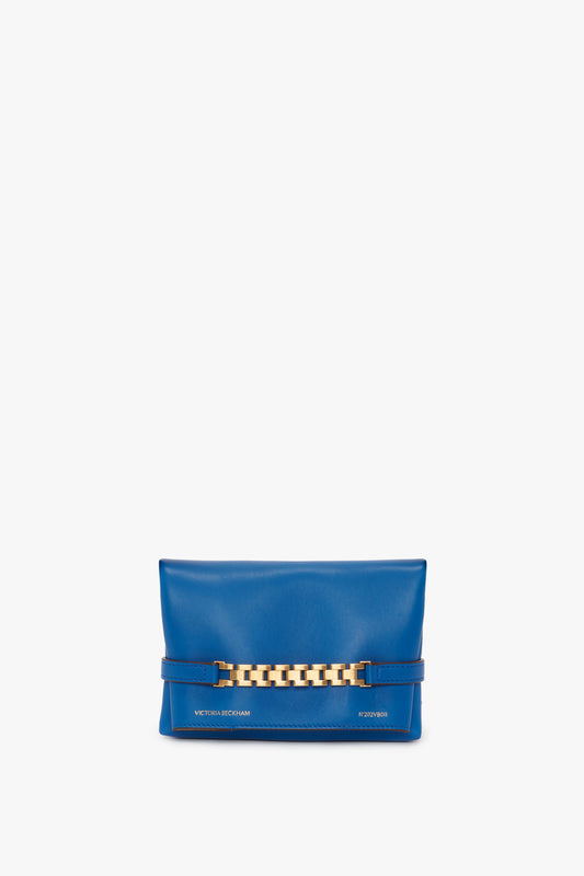 A Mini Chain Pouch Bag With Long Strap In Sapphire Blue with a gold chain detail on the front. The bag has "Victoria Beckham" written in gold lettering at the bottom, adding to its elegance.