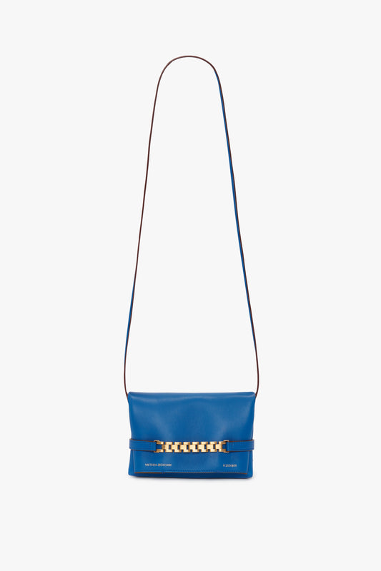 A sapphire blue leather shoulder bag with a long strap and a gold chain detail on the front, resembling a chic Mini Chain Pouch Bag With Long Strap In Sapphire Blue from Victoria Beckham.