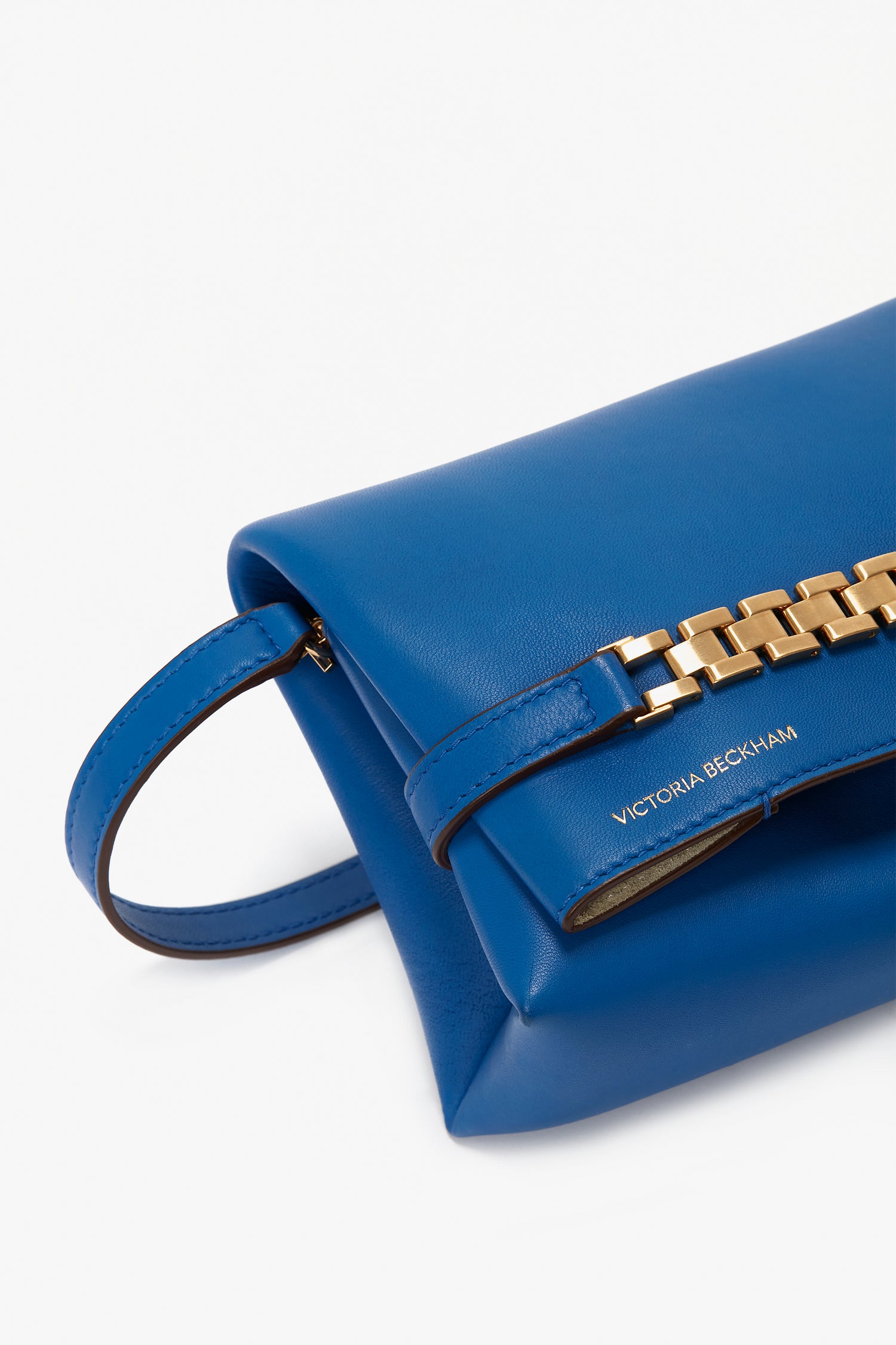 A Mini Chain Pouch Bag With Long Strap In Sapphire Blue with a gold chain detail and a handle, featuring the text "Victoria Beckham" embossed on the side.