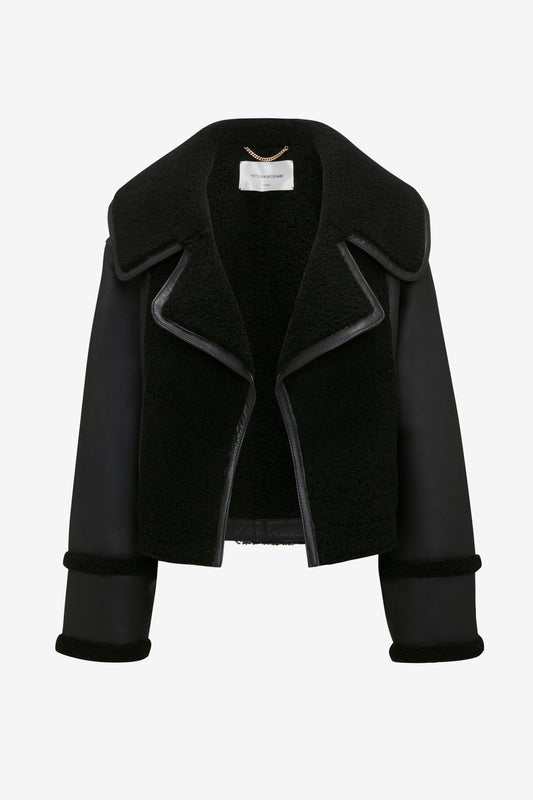 A Victoria Beckham Shearling Jacket In Black with wide lapels, open front, and folded cuffed sleeves. The inside is lined with a thick, textured material, showcasing its modern classic appeal.