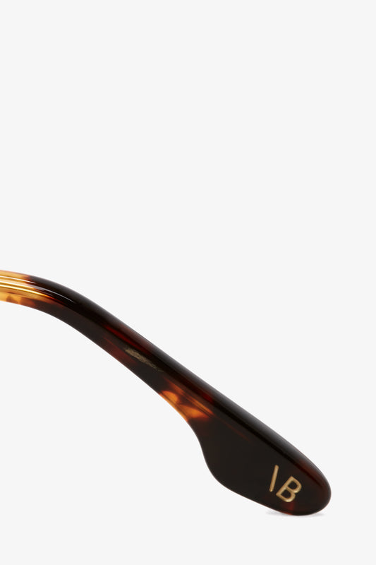 Close-up of a brown tortoiseshell eyeglass arm crafted from Dark Havana tortoise acetate, featuring the initials "IB" engraved in gold. These are the Guilloche Frame Opticals In Dark Havana by Victoria Beckham.