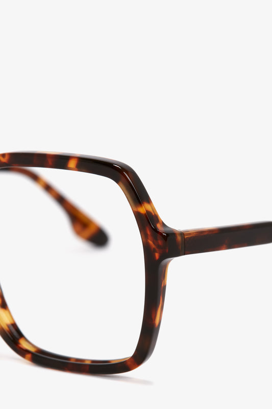 Close-up of a pair of Victoria Beckham Guilloche Frame Opticals In Dark Havana with lightweight rectangular frames made from Dark Havana tortoise acetate, set against a plain white background.