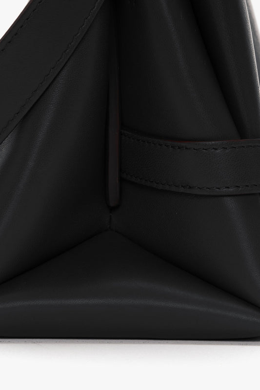 Close-up of a Victoria Beckham Chain Pouch Bag with Strap In Black Leather with neatly stitched seams, a triangular fold design, and a detachable handle.