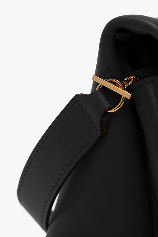 Close-up of a Chain Pouch Bag with Strap In Black Leather by Victoria Beckham, featuring a black Nappa leather strap attachment with a gold ring and buckle detail, and a detachable handle.