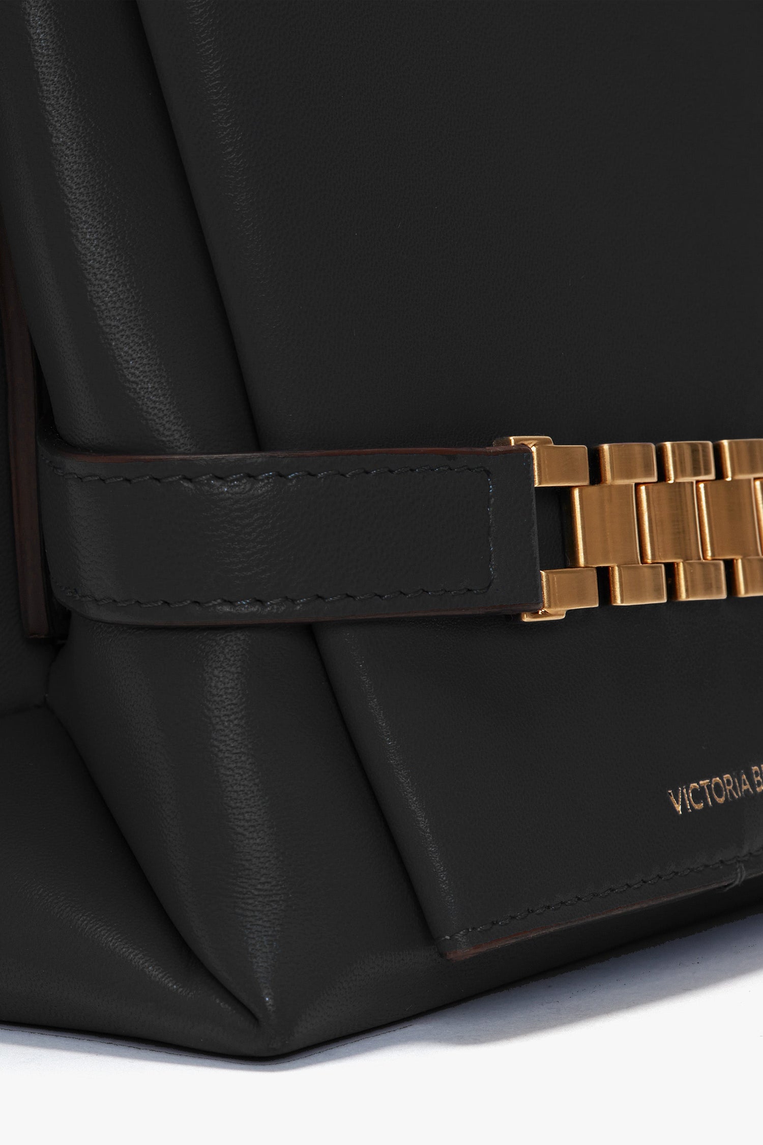 Close-up of a black Nappa leather Chain Pouch Bag with Strap In Black Leather by Victoria Beckham with a gold rectangular buckle, a small logo in the bottom right corner, and a sophisticated detachable handle.